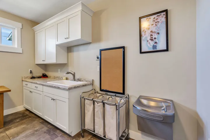 Utility room featuring wood-finish flooring, white cabinetry with crown molding, a countertop with an integrated sink, and a wall-mounted drinking fountain