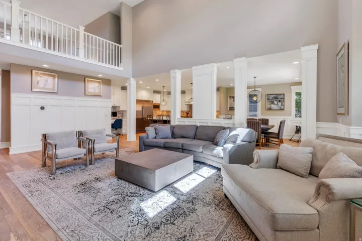 Spacious living area featuring high ceilings, wood-finish flooring, a white panel accent wall, and a balcony with white railings