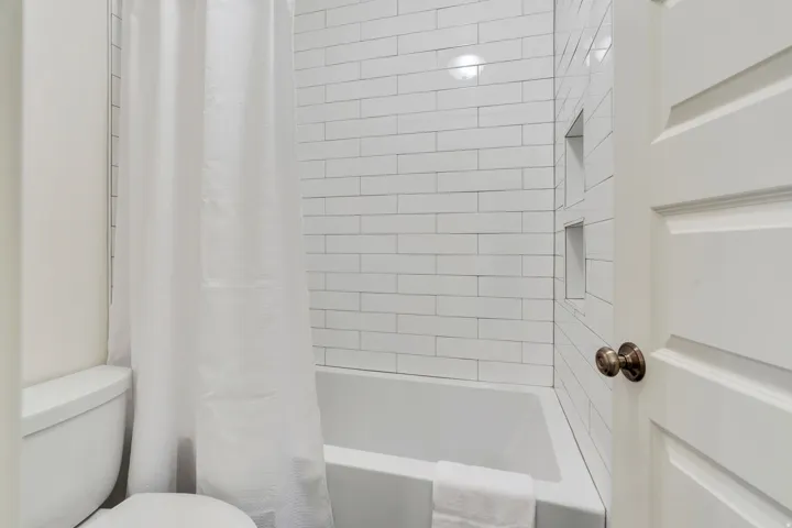 Bathroom featuring a white subway tile surround, integrated shower niches, a standard bathtub, and a paneled door with bronze hardware