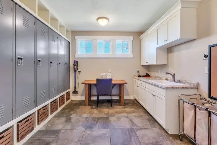 Utility room featuring extensive storage lockers, built-in shelving, durable tile flooring, white cabinetry, and a countertop with an integrated sink