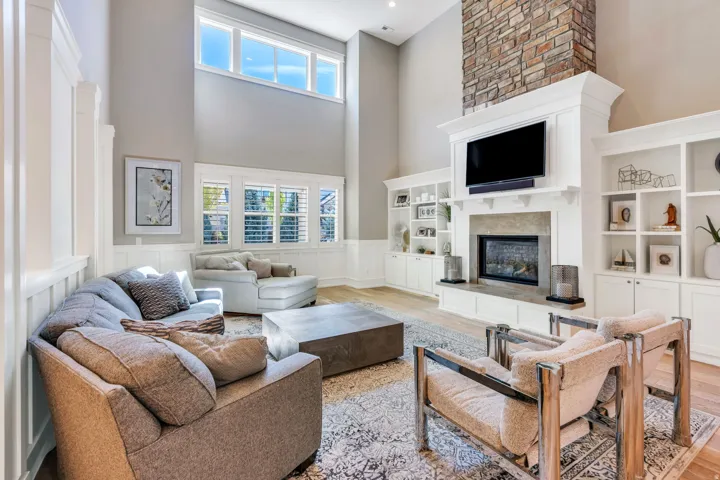 Two-story living area featuring a stone-clad fireplace with a built-in entertainment center, high ceilings, wood-finish flooring, and extensive built-in shelving