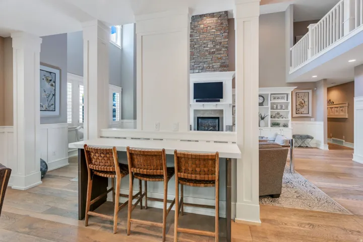 Breakfast bar with a light-toned countertop, wood-finish flooring, white wainscoting, and a stone-faced fireplace with a white mantel