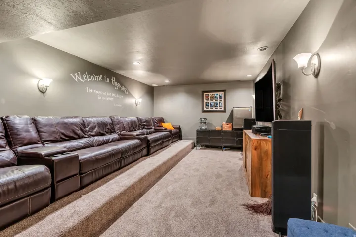 Spacious media room featuring tiered carpeted flooring, recessed lighting, and wall-mounted sconces