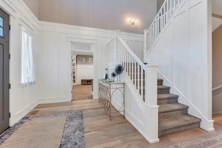 Entryway featuring wood-finish flooring, white wainscoting, and a carpeted staircase with white railings