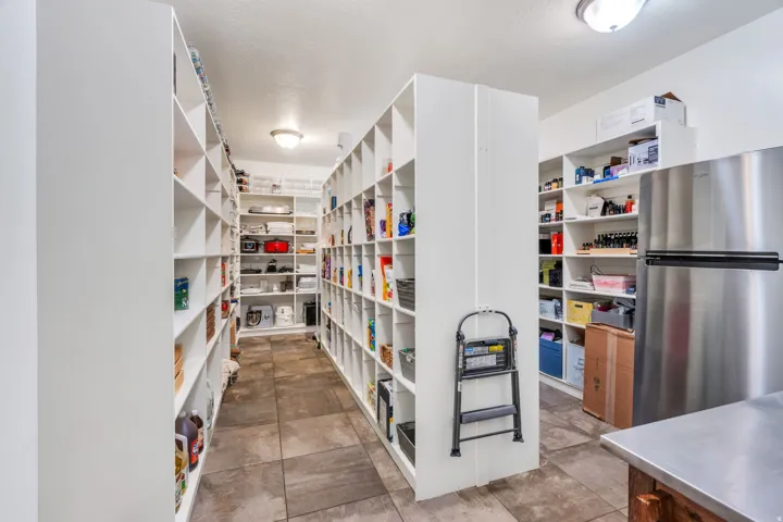 Spacious pantry featuring extensive built-in white shelving, recessed lighting, and large format tile flooring