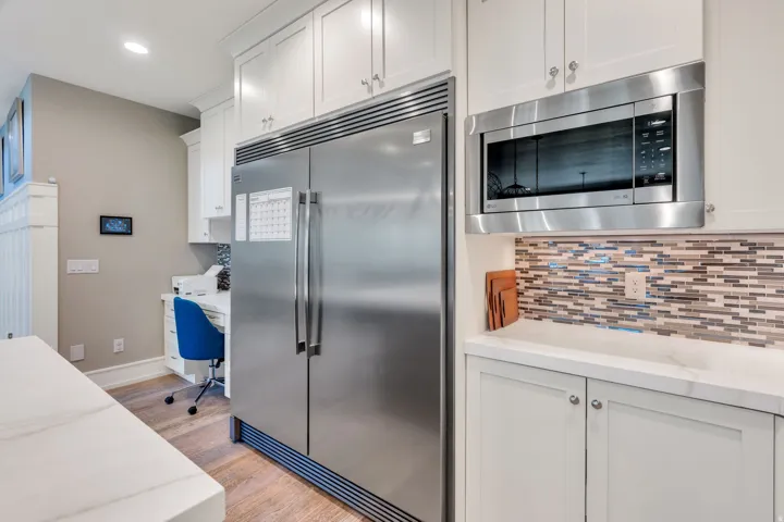 Stainless steel side-by-side refrigerator, built-in microwave, white shaker cabinetry, and a mosaic tile backsplash