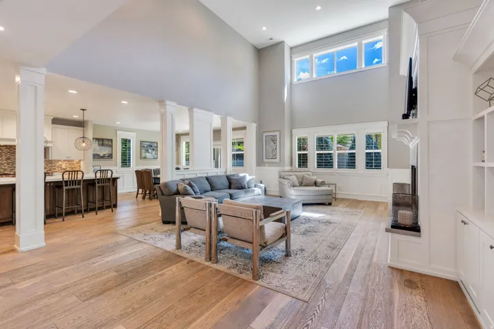 Expansive living area featuring high ceilings, light wood-finish flooring, and multiple windows with plantation shutters