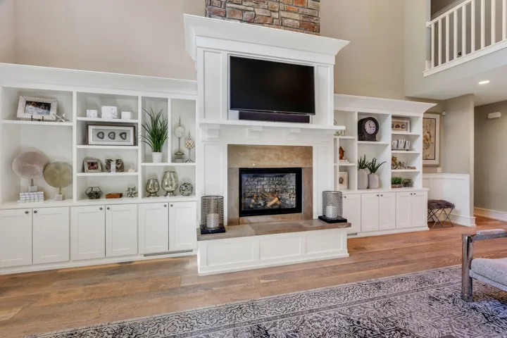 Built-in entertainment center featuring extensive white cabinetry, open shelving, a stone-faced fireplace surround, and wood-finish flooring