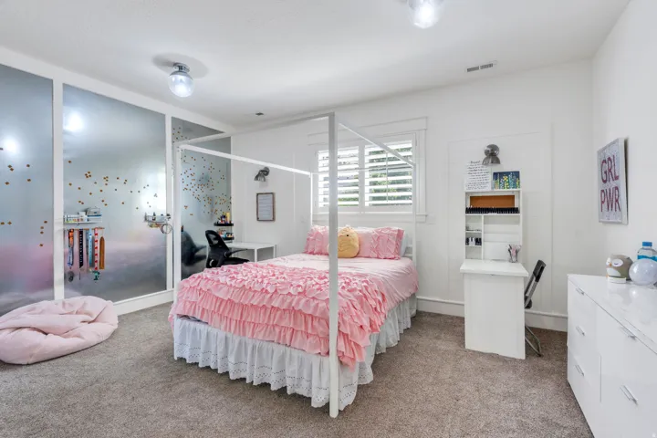 Carpeted room featuring a window with white plantation shutters, built-in shelving, and a wall-mounted desk