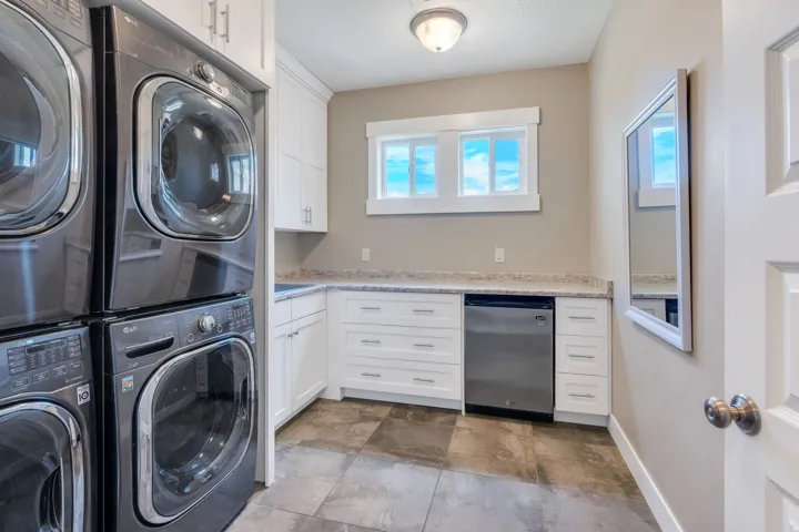 Laundry area featuring stacked front-load washers and dryers, white cabinetry with silver hardware, light-toned countertop, and tile flooring