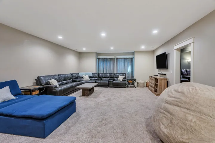 Spacious recreation area featuring plush carpet flooring, recessed lighting, and a light gray wall color