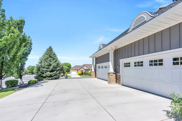 Spacious concrete driveway leading to a multi-car garage with white paneled doors featuring decorative windows