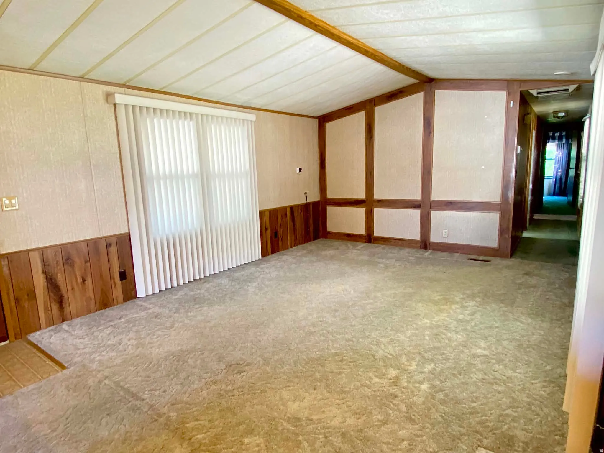 Carpeted living space featuring vertical blinds, paneled walls, and wood-finish ceiling beams