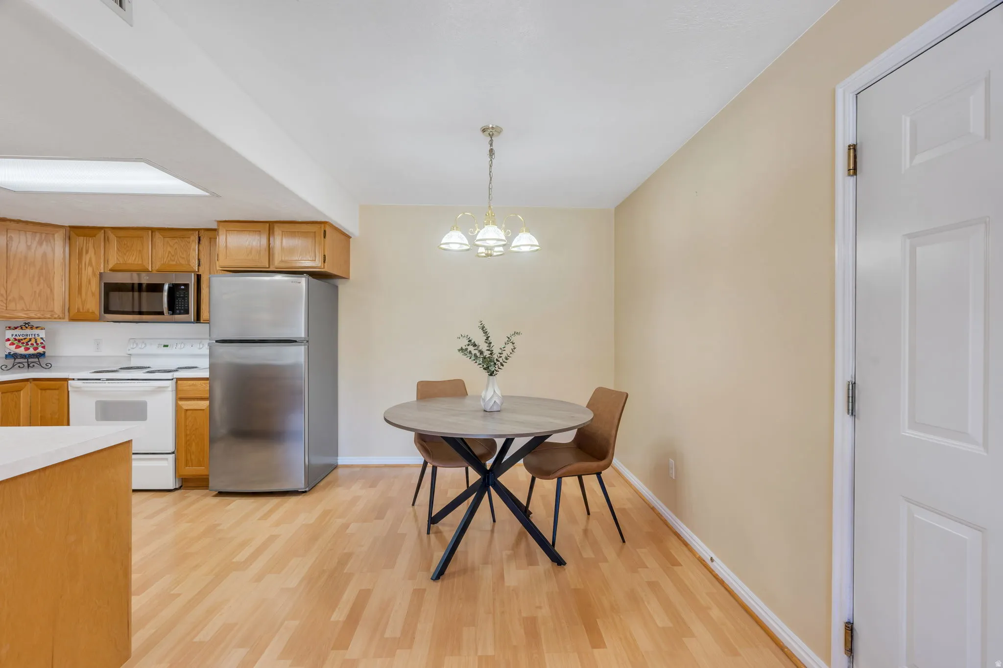 Open-concept kitchen and dining area featuring wood-finish flooring, light wood cabinetry, white countertops, and stainless steel appliances