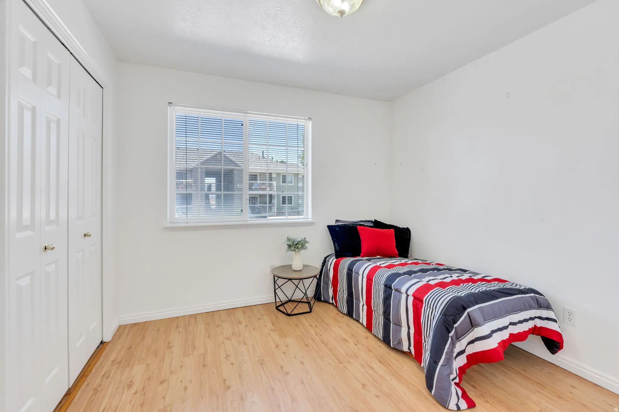 #1 Bedroom featuring wood-finish flooring, a double-door closet with gold-tone hardware, a window with horizontal blinds, and a flush-mount ceiling light