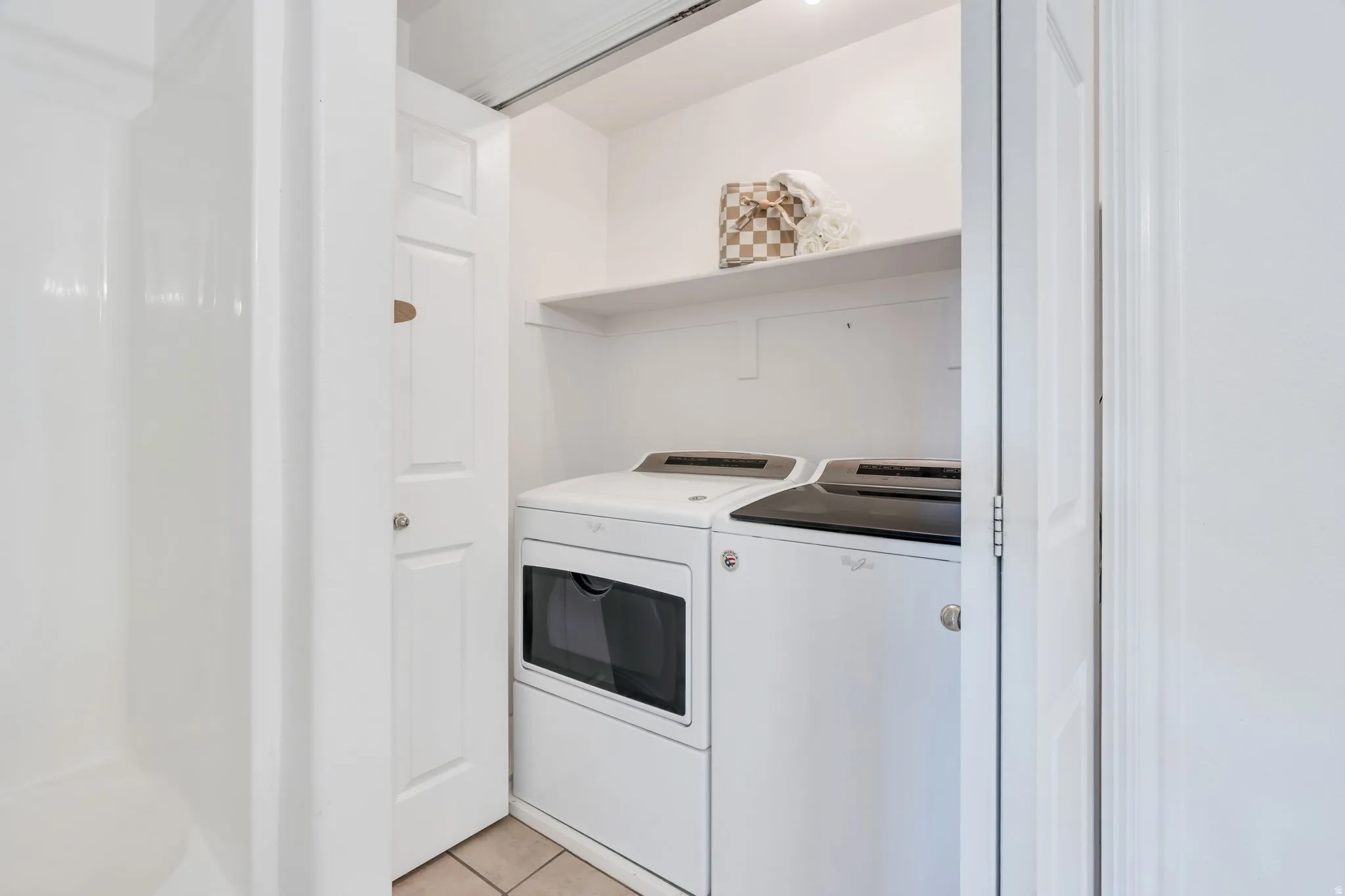 Dedicated laundry area featuring a stacked washer and dryer (included), white shelving, and light-toned tile flooring