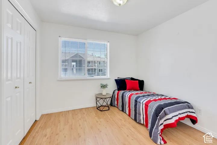 #1 Bedroom featuring wood-finish flooring, a double-door closet with gold-tone hardware, a window with horizontal blinds, and a flush-mount ceiling light