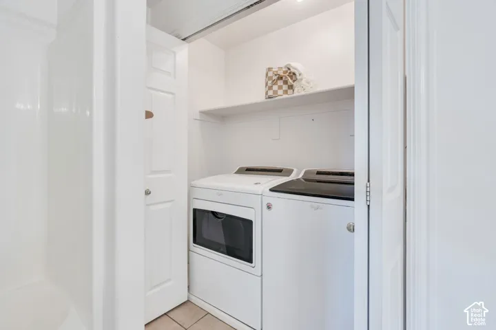 Dedicated laundry area featuring a stacked washer and dryer (included), white shelving, and light-toned tile flooring