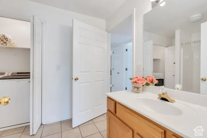 Inside of Bathroom featuring a single vanity with a white countertop and integrated sink, a large wall-mounted mirror, and tile flooring