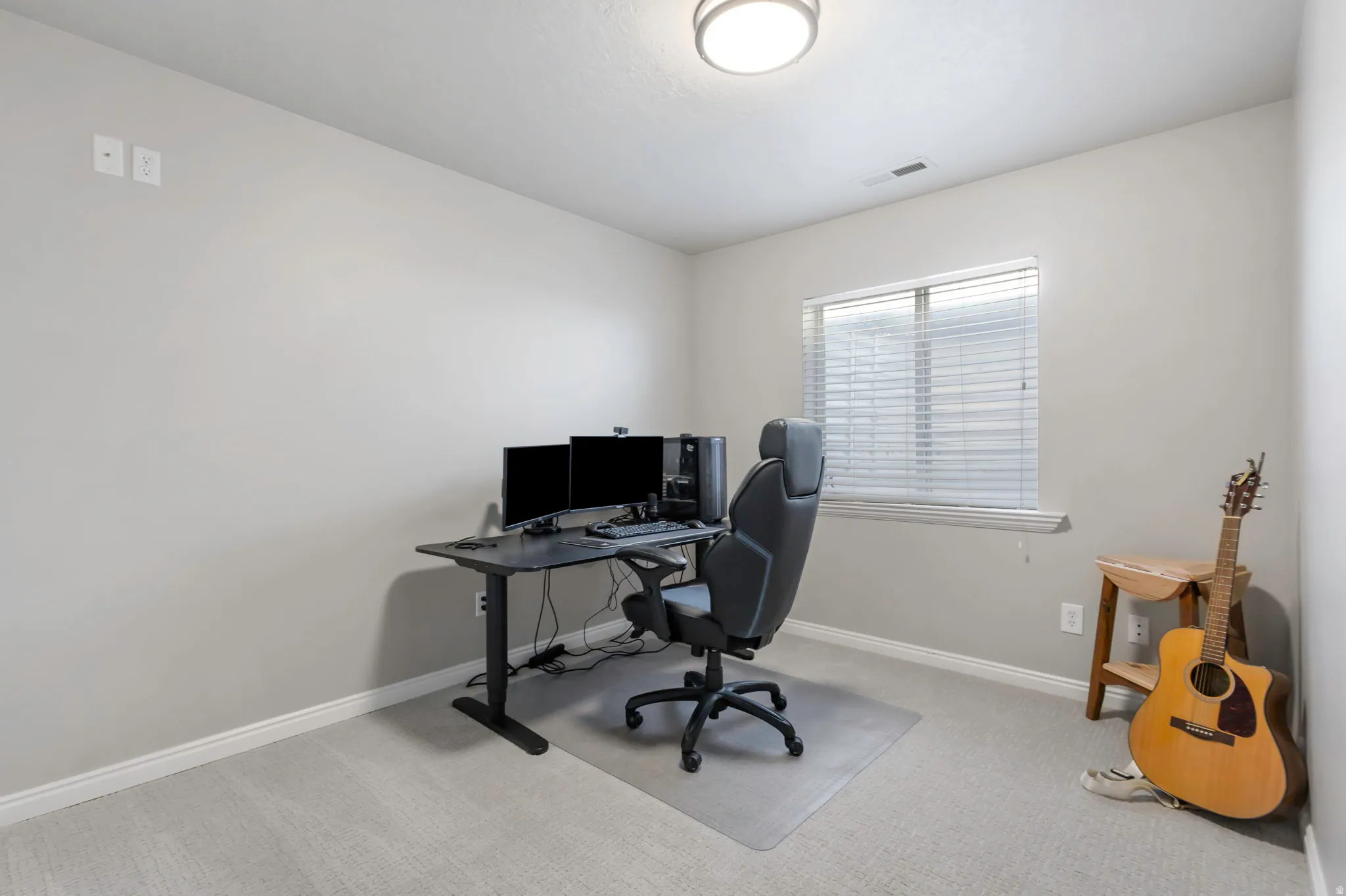 Neutral gray wall finishes provide a versatile backdrop to this space, featuring light-colored carpet, white baseboards, and a single window with blinds