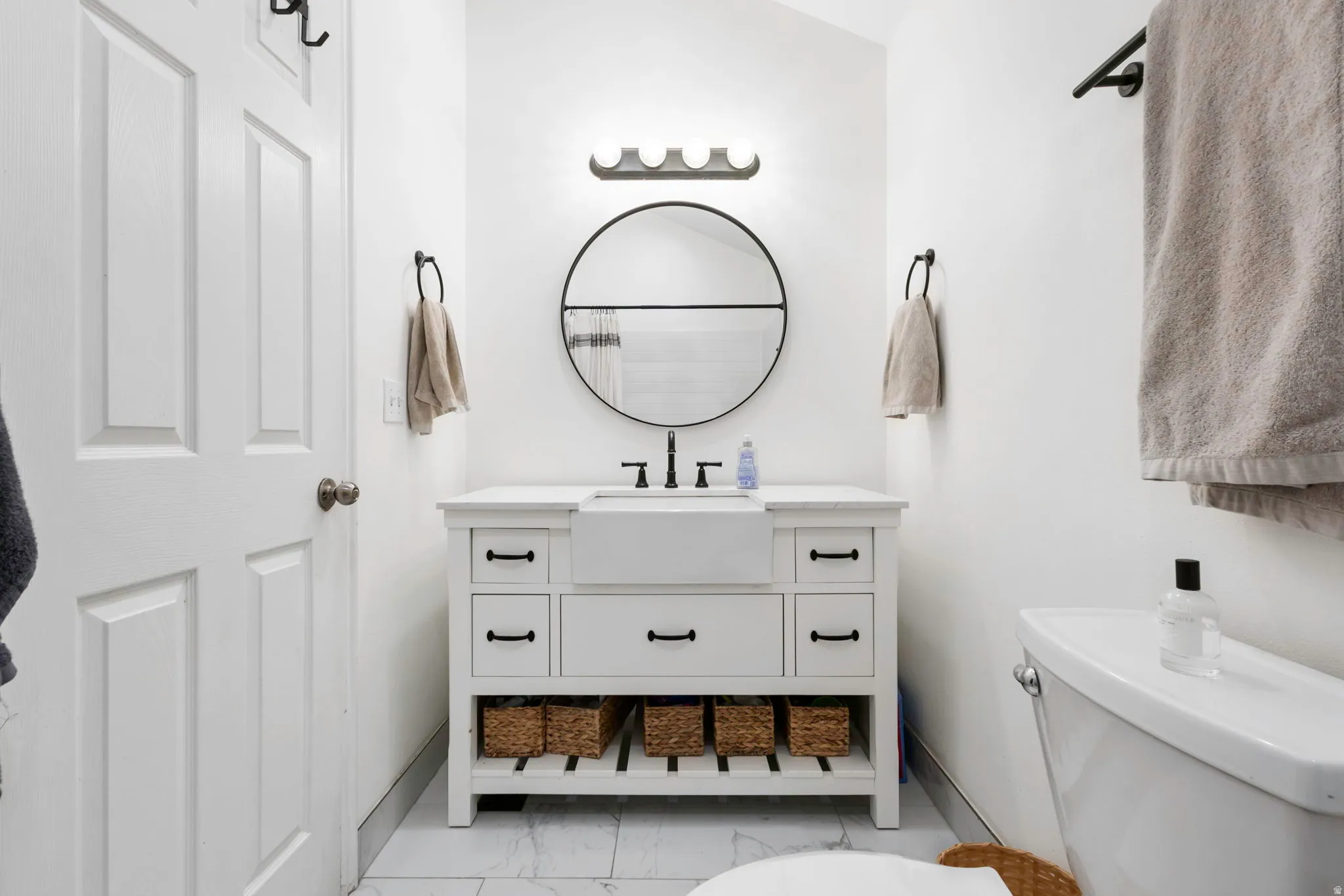 White vanity with a farmhouse sink, black hardware, and open shelving