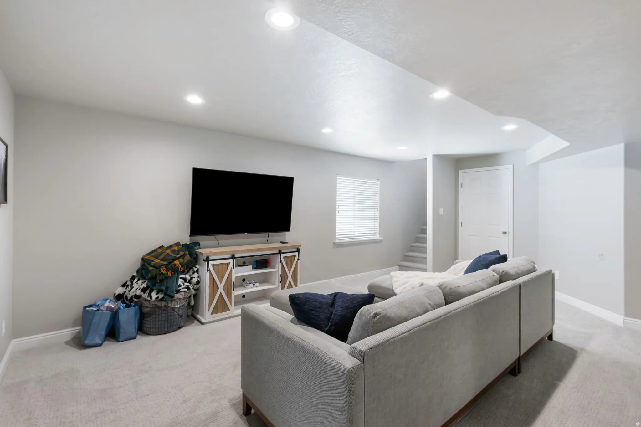 Recessed lighting illuminates this carpeted room featuring light gray walls, a window with blinds, and white trim