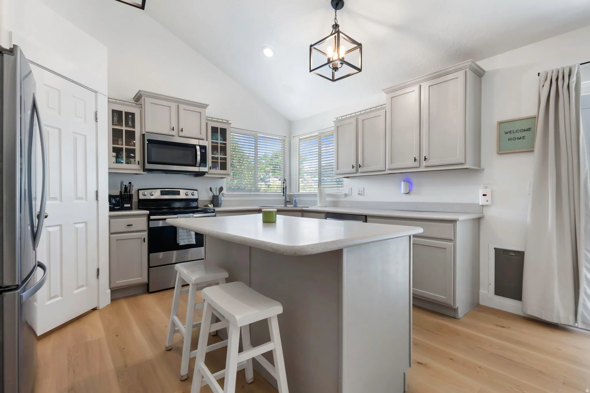 Bright kitchen featuring a central island with countertop seating, wood-finish flooring, vaulted ceilings, and light-toned cabinetry