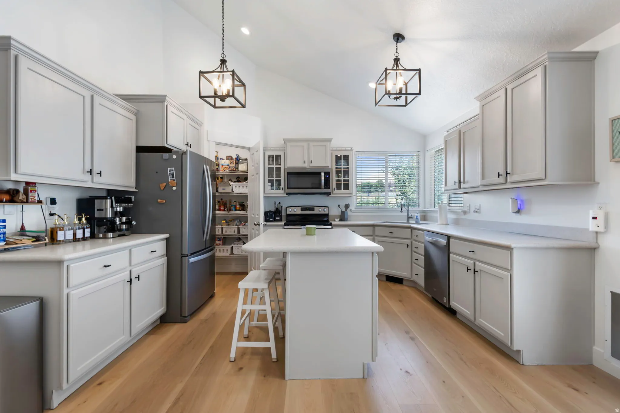 Kitchen featuring vaulted ceilings, light wood-finish flooring, a central island with countertop seating, stainless steel appliances, and a full-size pantry