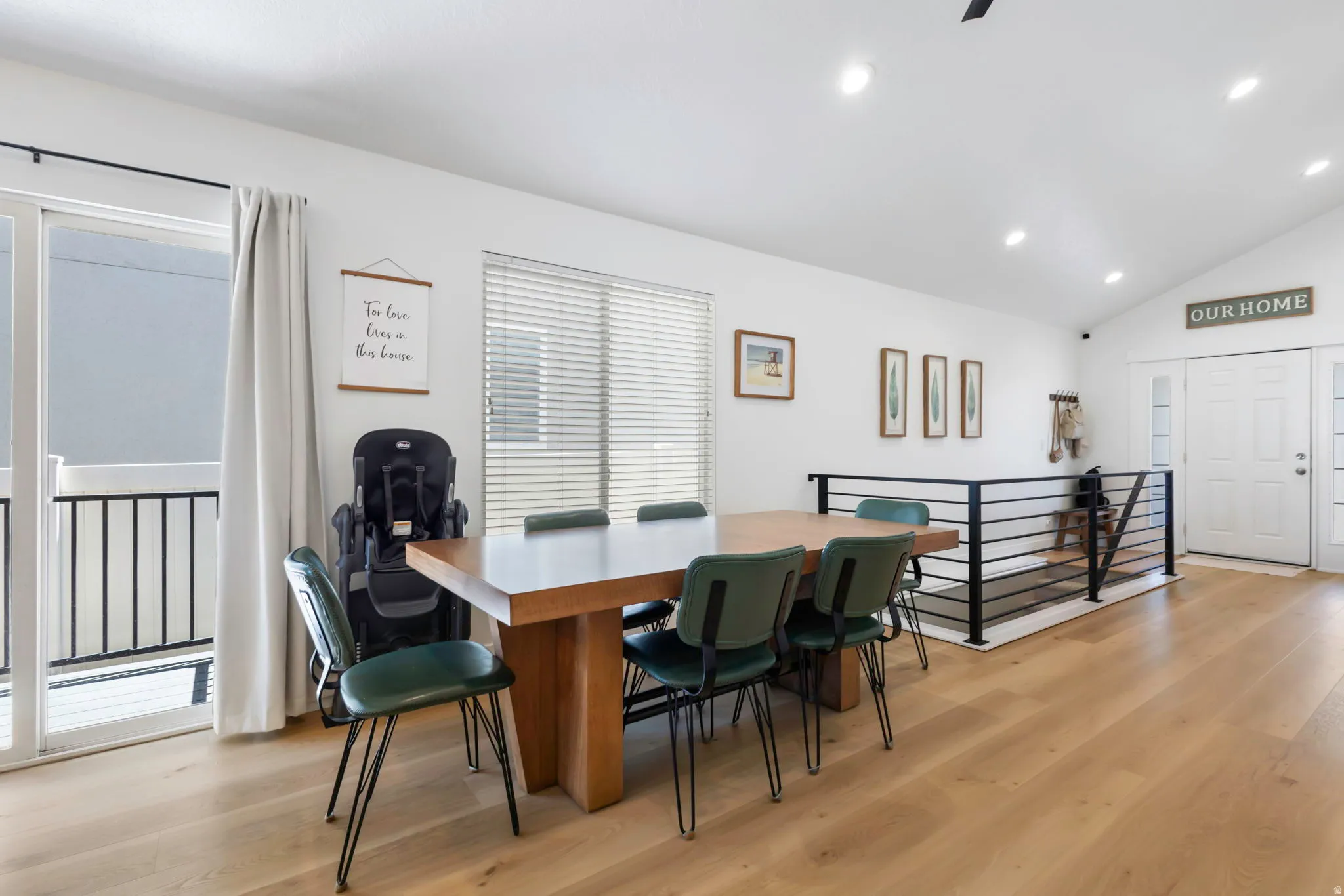 Open-concept living area featuring light wood-finish flooring, a contemporary black metal railing, a vaulted ceiling, recessed lighting, and a sliding glass door leading to a balcony