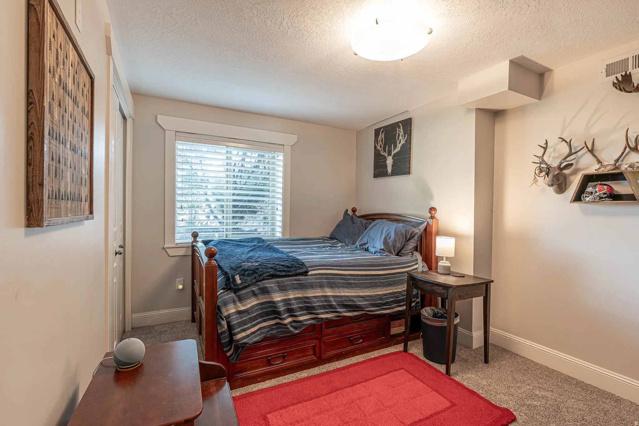 Spacious basement bedroom featuring light neutral wall paint, a window with blinds, and new plush carpet flooring