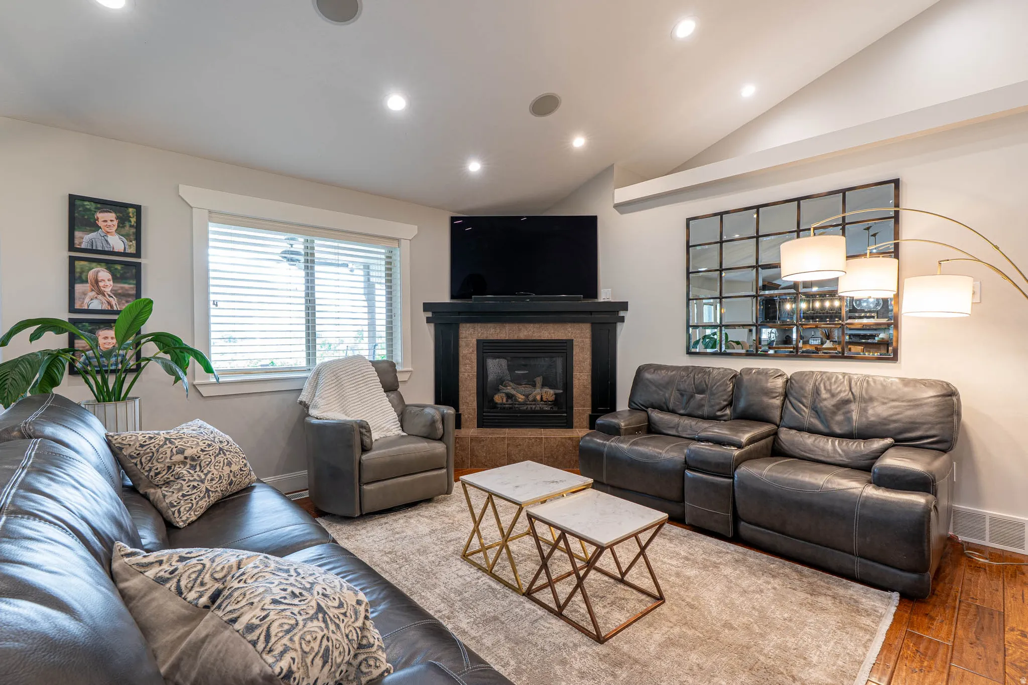 Living area featuring a fireplace with a black mantel and tile surround, recessed lighting, vaulted ceilings, and wood-finish flooring
