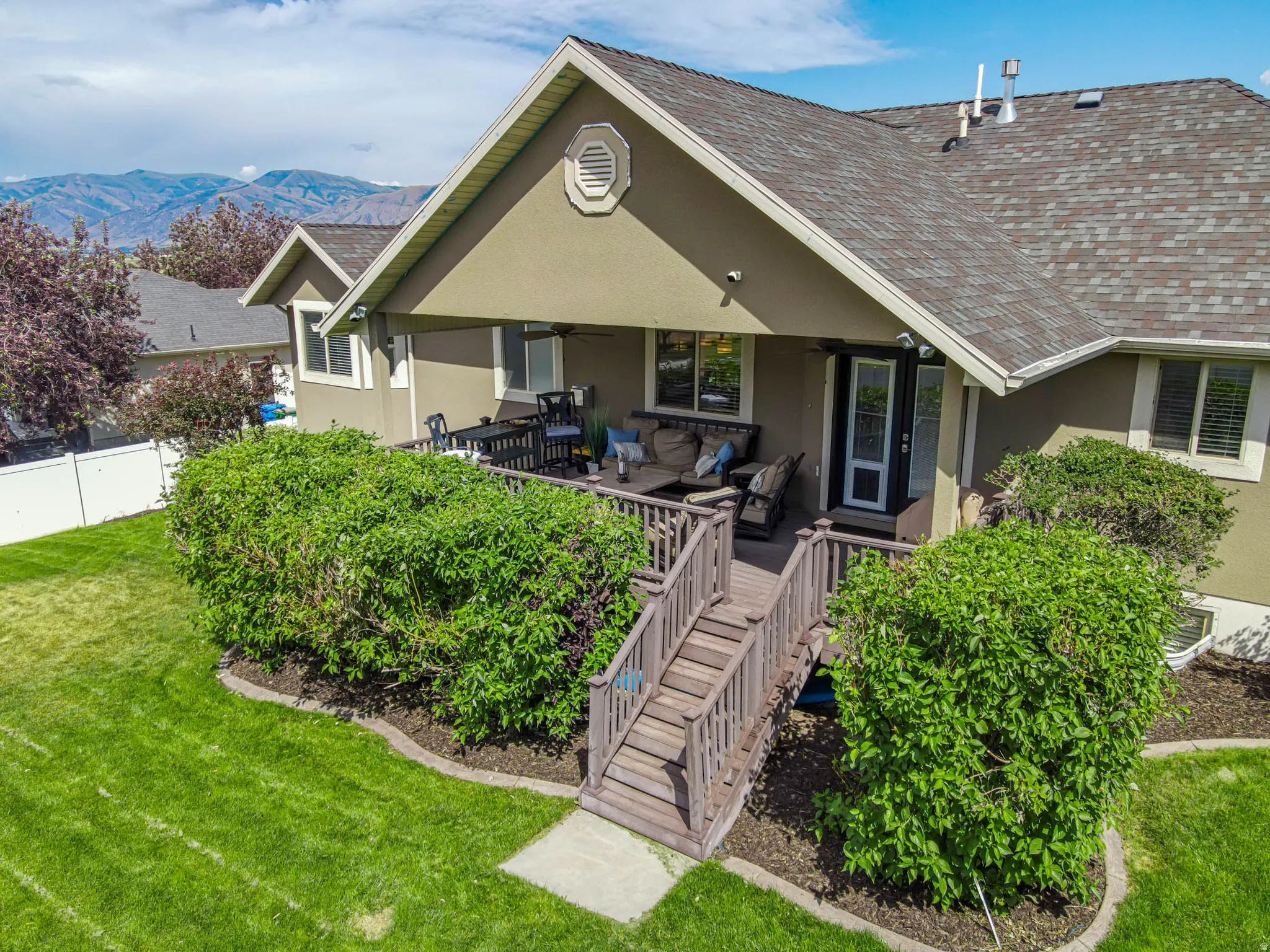 Rear exterior featuring a covered deck, wood-tone Trex decking, and stairs descending to a beautiful backyard