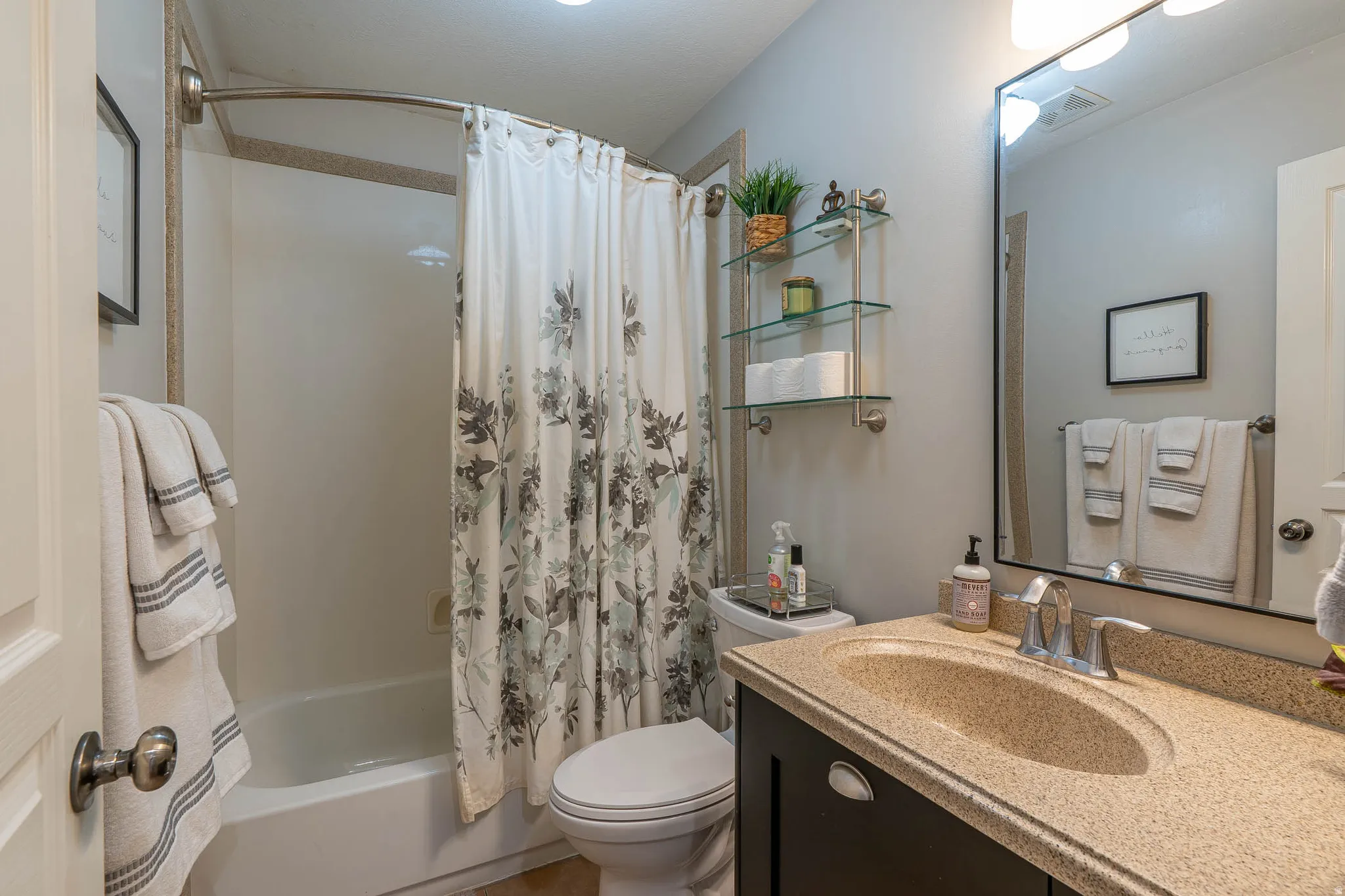First floor bathroom featuring a built-in tub with shower, single vanity with integrated sink, dark wood-finish cabinetry, and a large wall mirror