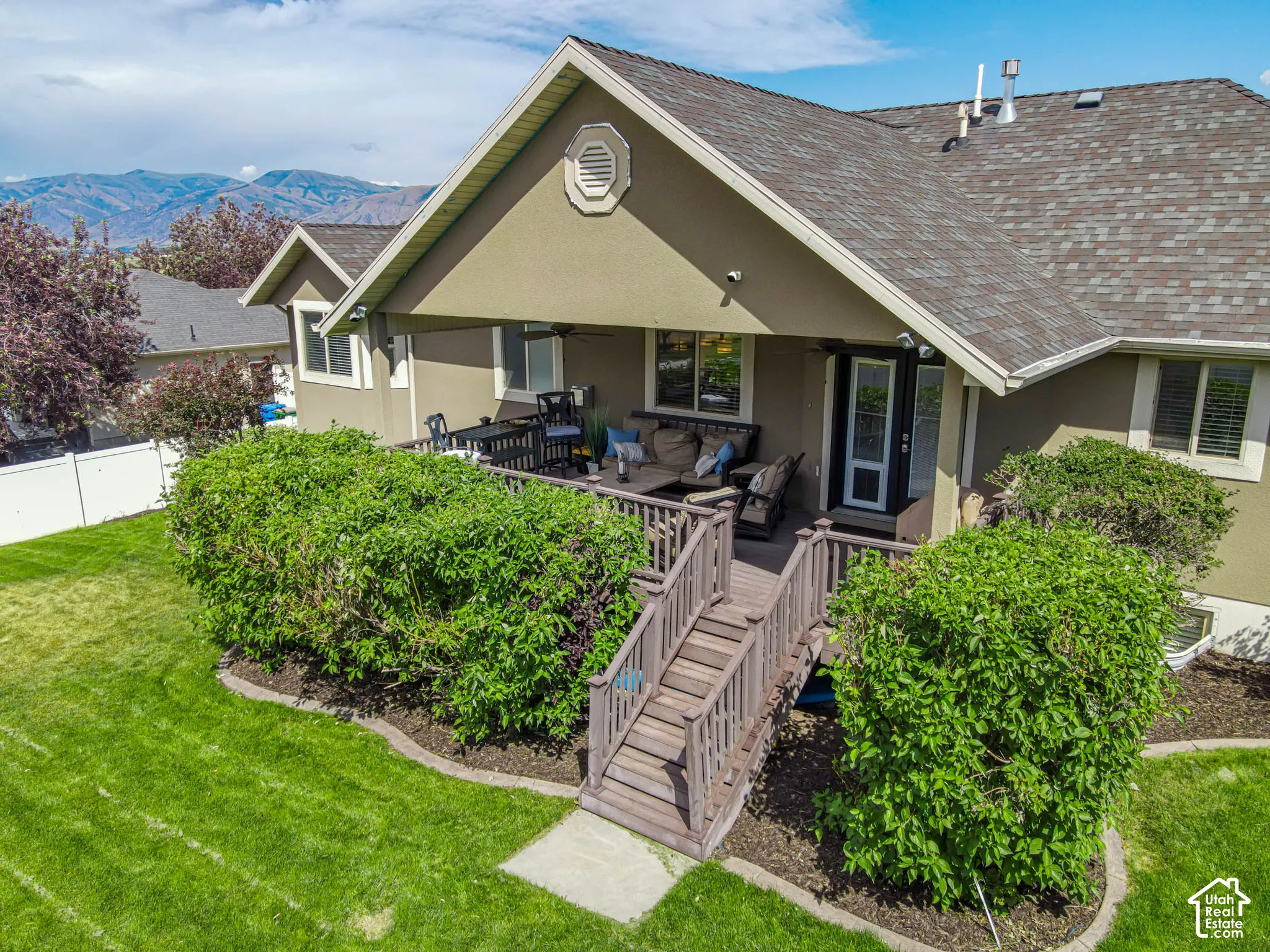 Rear exterior featuring a covered deck, wood-tone Trex decking, and stairs descending to a beautiful backyard