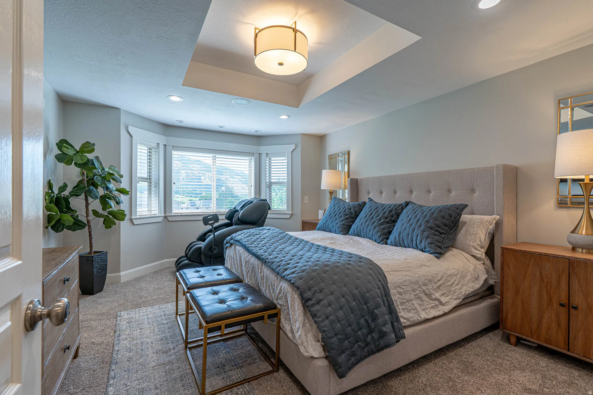 Spacious primary bedroom featuring a tray ceiling with a central drum pendant light and recessed lighting. Amazing views of the Wellsville Mountains from the bedroom window.