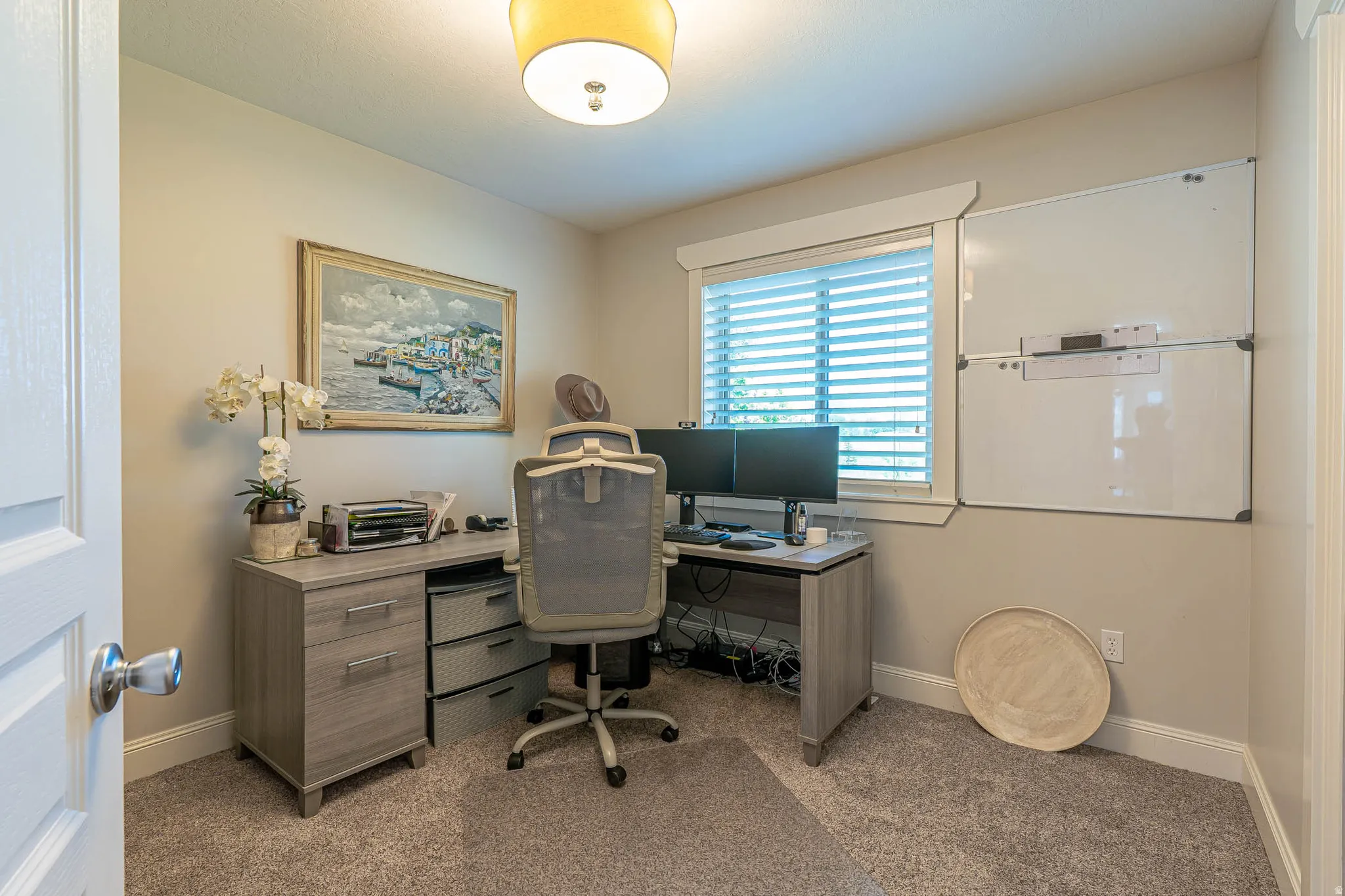 Bedroom featuring a window with blinds, neutral-toned walls, and a ceiling-mounted light fixture. Currently being used as an office.