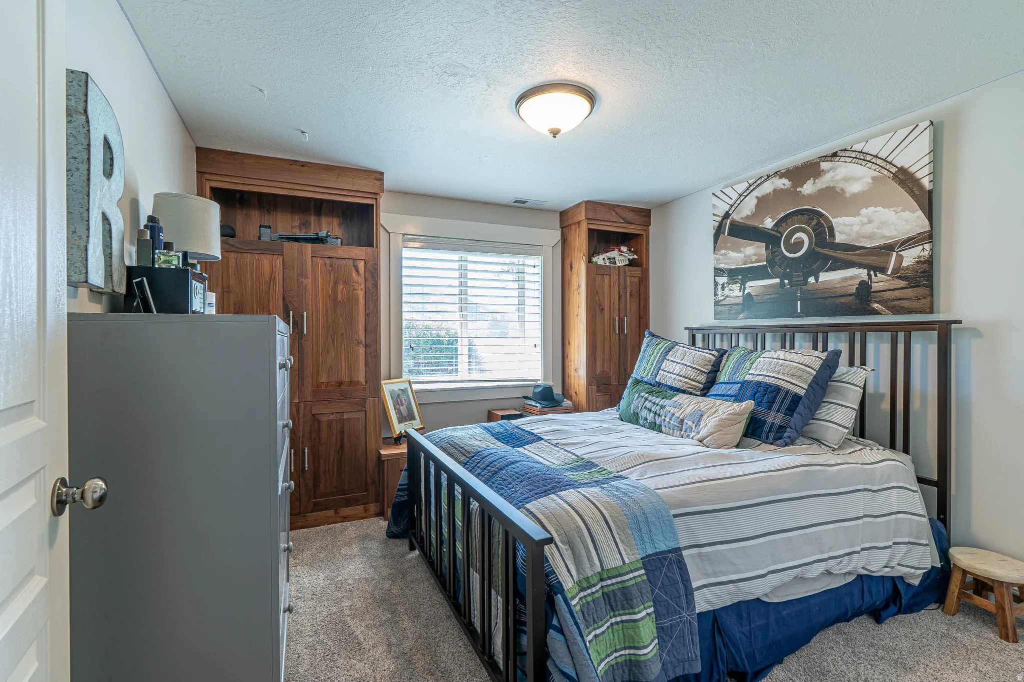 Basement bedroom featuring built-in wood cabinetry, a window with horizontal blinds, and a flush-mount ceiling light fixture
