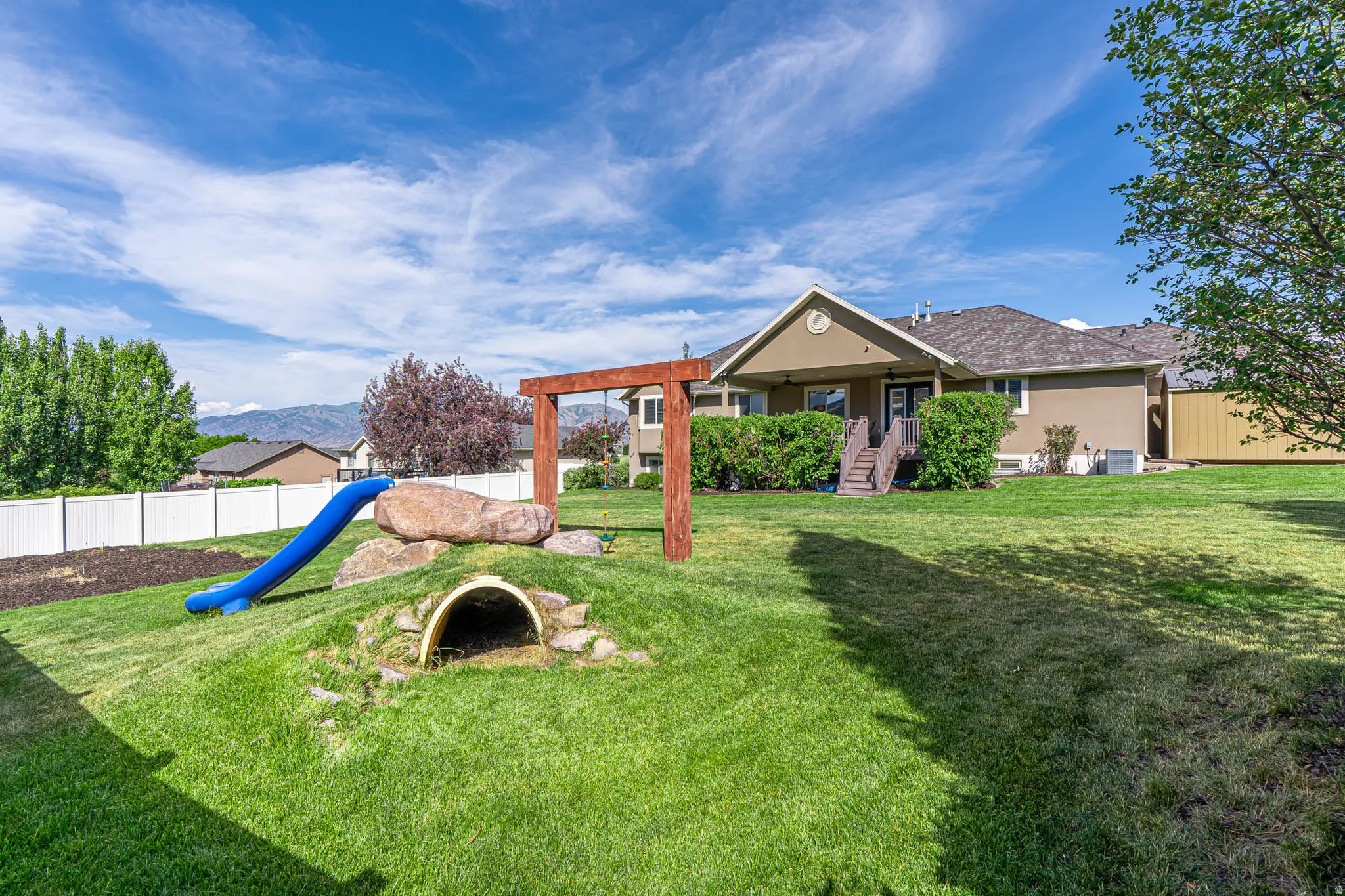 Expansive backyard featuring a manicured lawn, a white privacy fence, room for garden and a stucco exterior with a covered patio