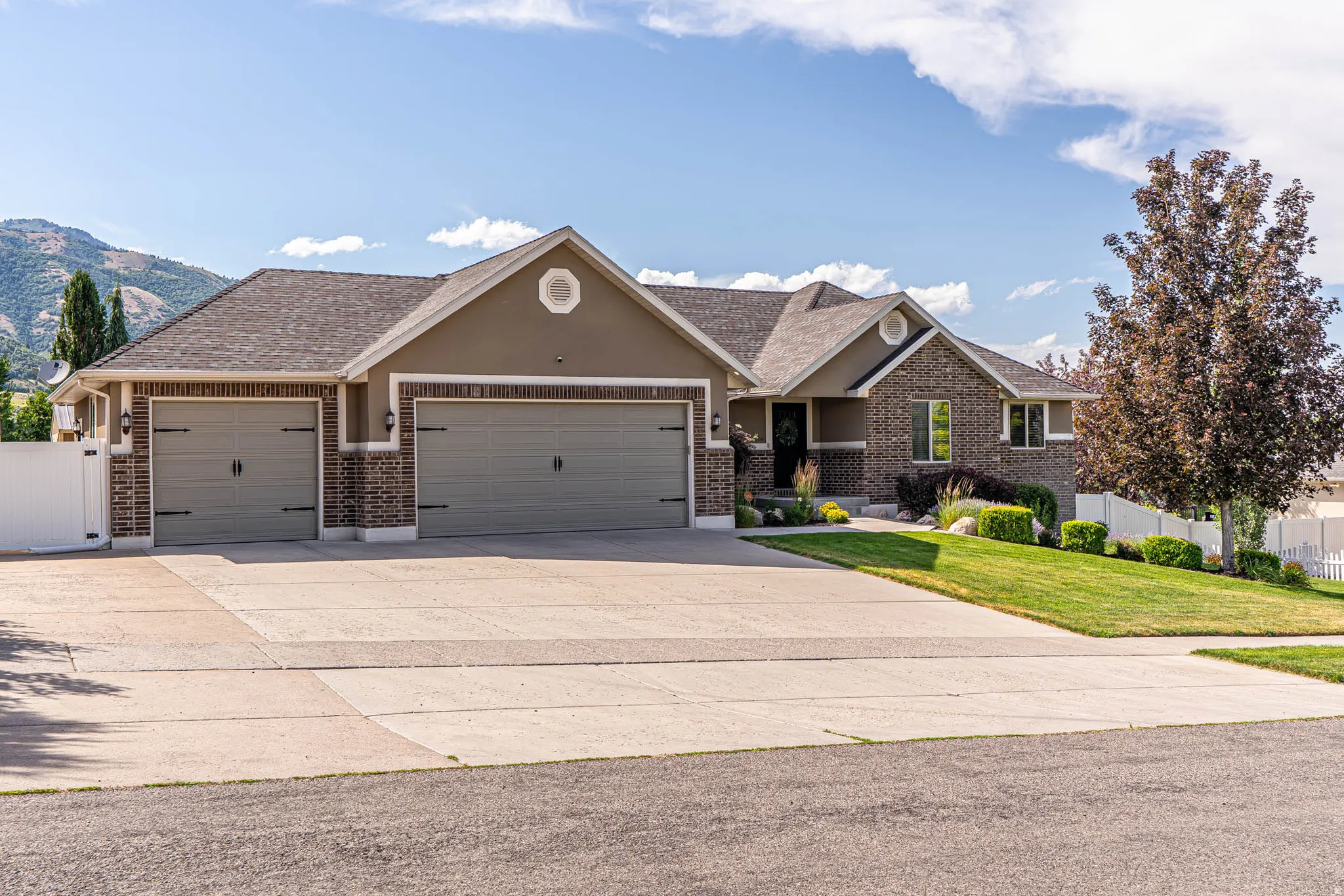 Contemporary ranch-style residence featuring a brick and stucco facade, a three-car garage with carriage-style doors, an oversized concrete driveway, and a manicured front lawn