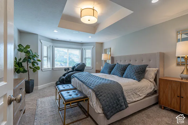 Spacious primary bedroom featuring a tray ceiling with a central drum pendant light and recessed lighting. Amazing views of the Wellsville Mountains from the bedroom window.