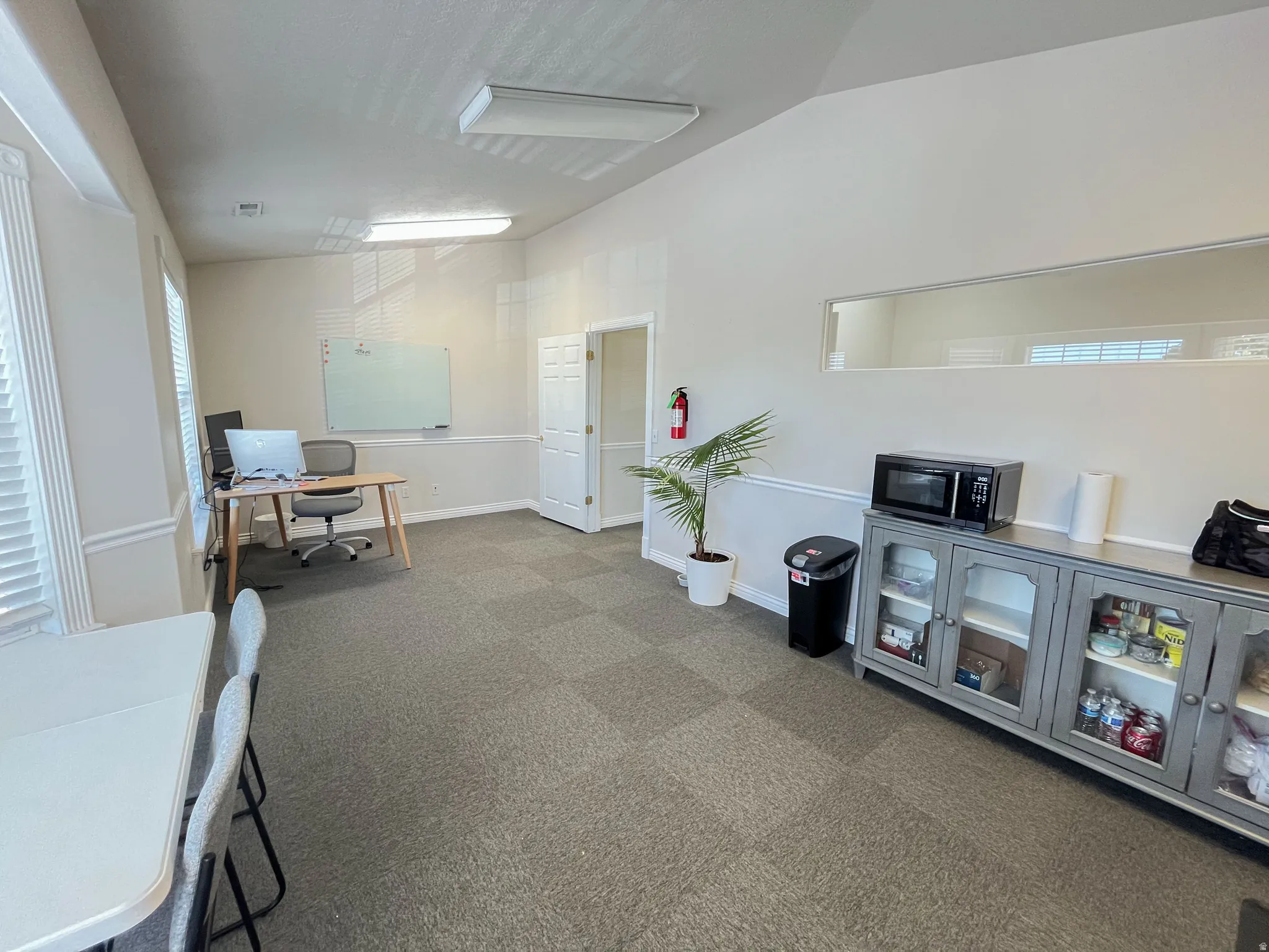 Spacious room featuring vaulted ceilings, a gray patterned carpet, and multiple windows with horizontal blinds