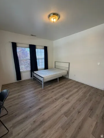 Spacious room featuring wood-finish flooring, two windows with blinds, a ceiling-mounted light fixture, and white wall finishes