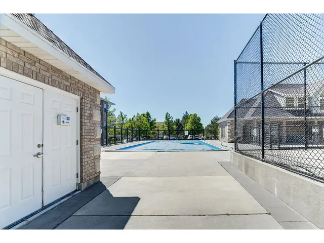Outdoor concrete patio area with a covered pool surrounded by a black chain-link fence