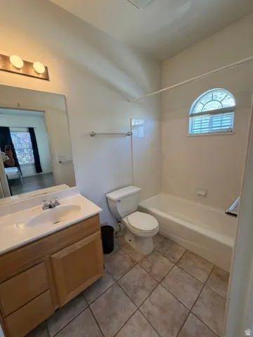 Bathroom featuring a wood-finish vanity with an integrated sink, a full-width mirror, tile flooring, a tub/shower combination, and an arched window with blinds