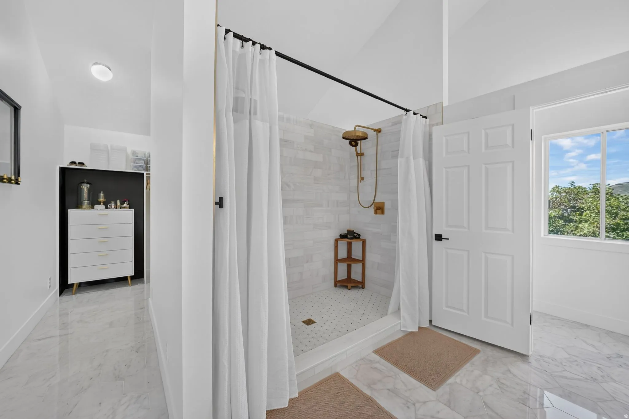 Shower enclosure with brass-finish fixtures, white subway tile surround, and a coordinating pebble-tile floor