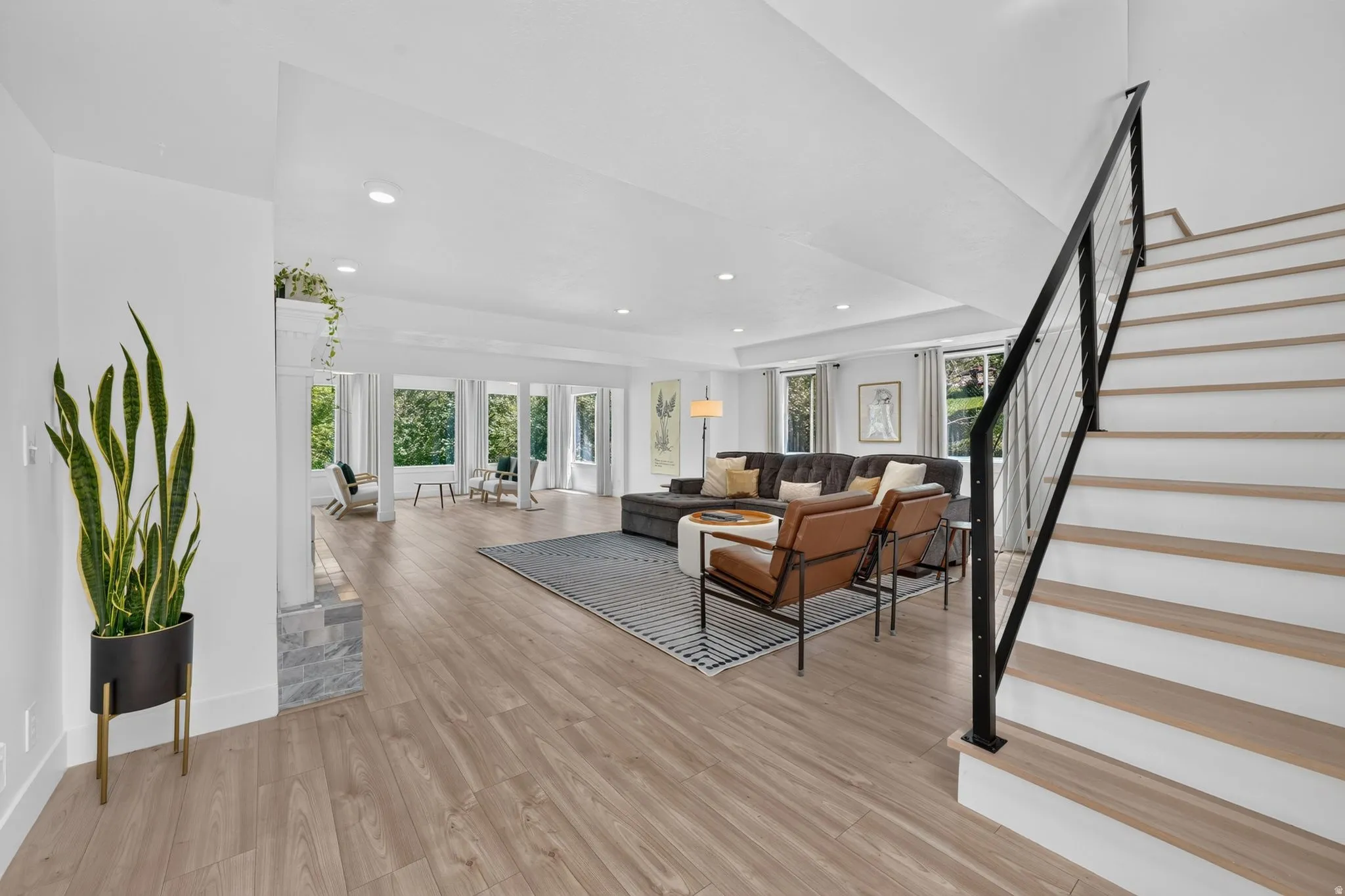 Open-concept living area with wood-finish flooring, recessed lighting, and a modern staircase featuring black metal railings and cable infill