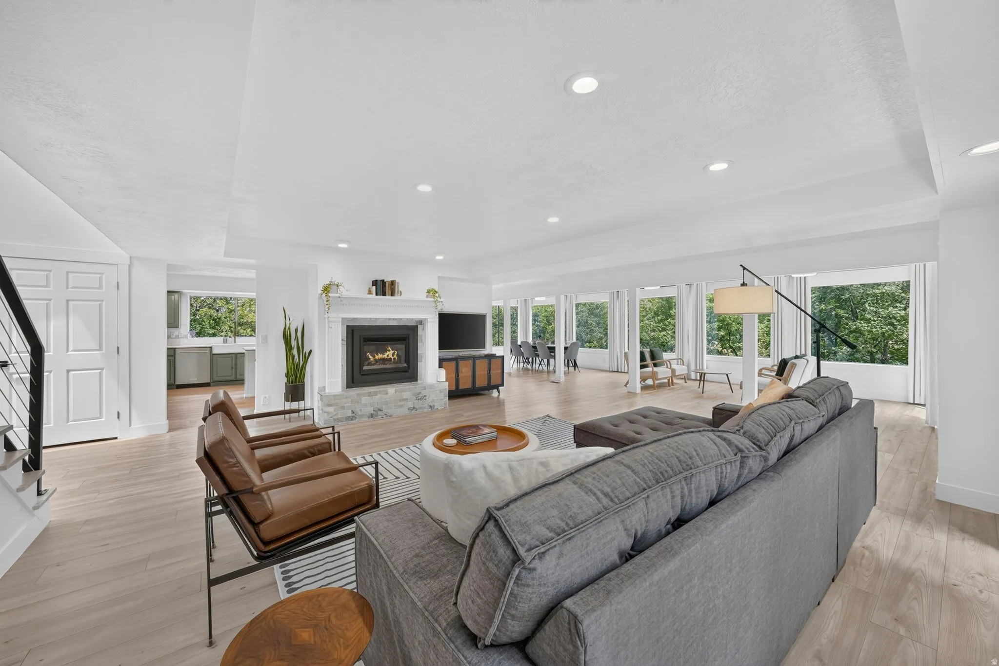 Spacious living area featuring light wood-finish flooring, recessed lighting, and a modern fireplace with a white mantel and stone surround