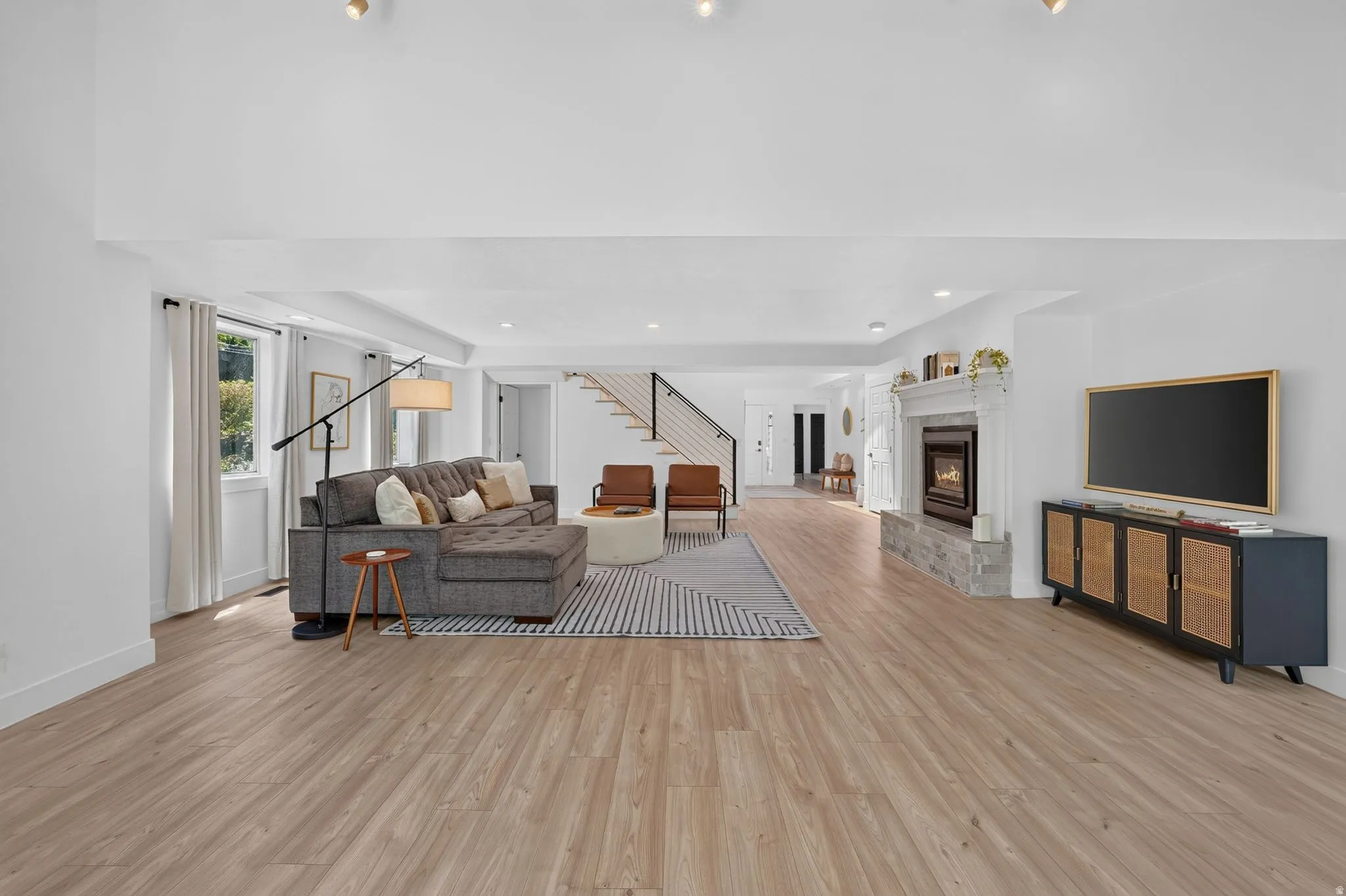 Spacious living area featuring wood-finish flooring, a stone-faced fireplace with a white mantel, and ample natural light from multiple windows