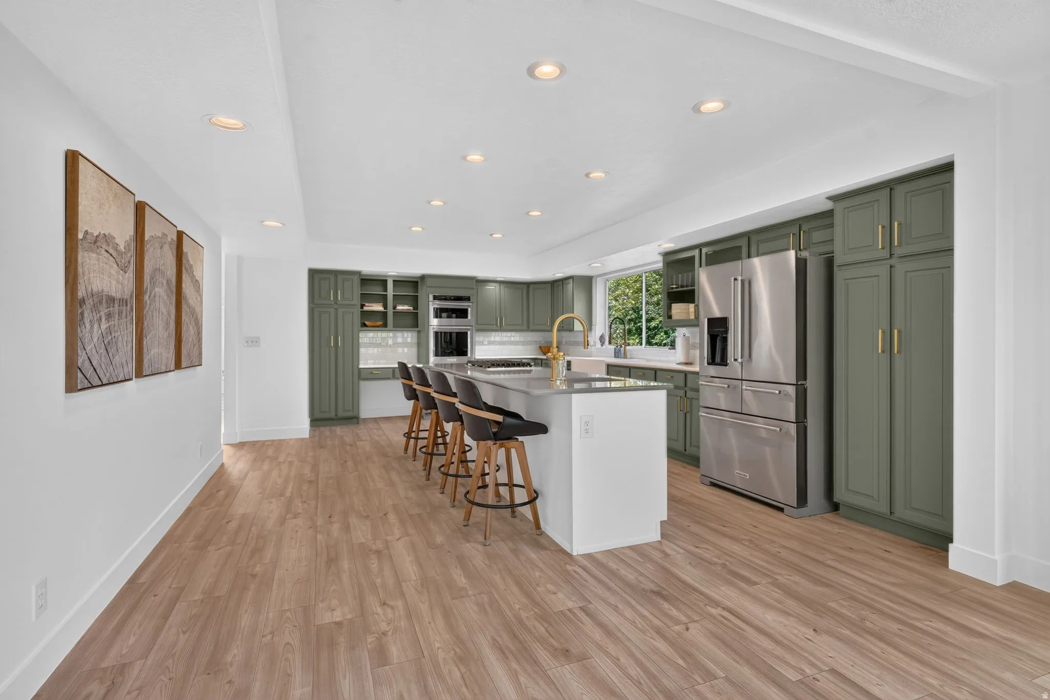Spacious kitchen featuring sage green cabinetry, stainless steel appliances, a large center island with seating, recessed lighting, and wood-finish flooring