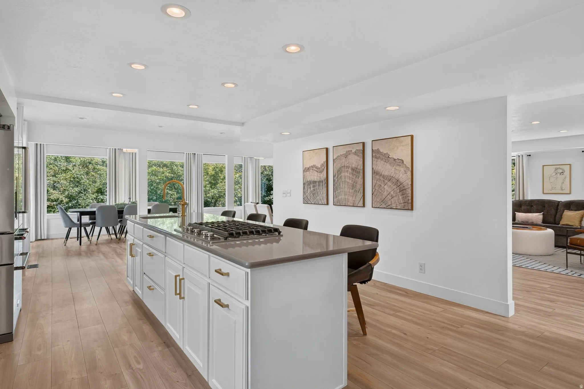 Kitchen island with integrated gas cooktop, light-toned wood-finish flooring, recessed lighting, and white cabinetry with brass hardware